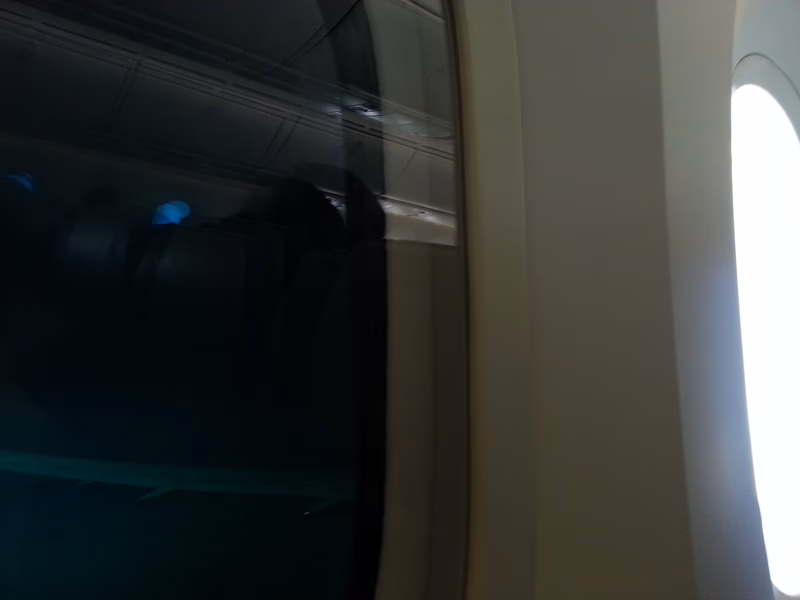 A photo of an airplane window with a view of the interior of an airplane seat.